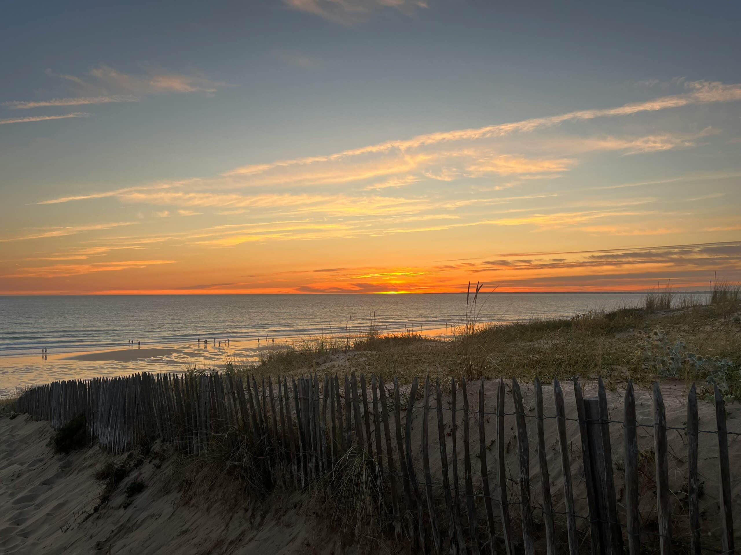 Serene sunset over a sandy beach and wooden fence at La Tranche-sur-Mer, France.